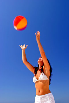 girl catching beach ball on sunny beach in spain with blue sky