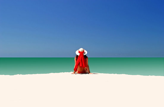 woman in red hat and bikini sitting all alone on empty beach