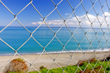 beautiful paradise beach seen through wires of a fence