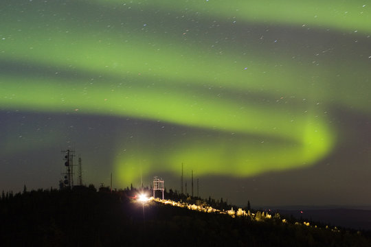 aurora borealis over hill with antennas and car wi