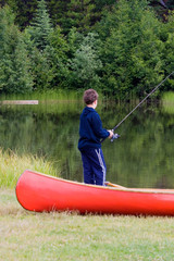 boy fishing in a lake beside his canoe