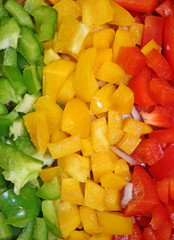 Lines of freshly chopped green, yellow, and red peppers filling the frame, showcasing vibrant colour, freshness, and healthy natural ingredients.