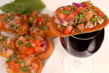 bruschetta resting on a glass of wine with additional bruschetta