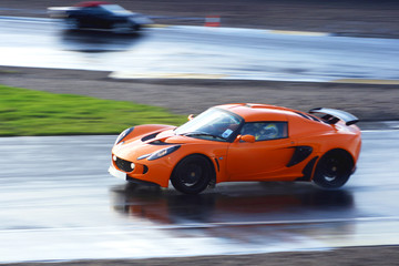 orange sports car on wet race circuit