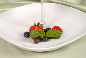 fresh berries with mint surrounding the stem of a glass