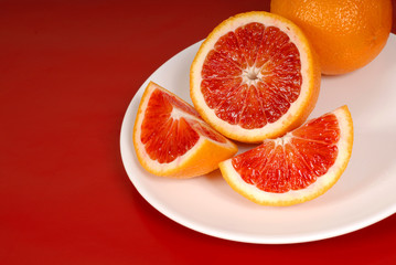 Fototapeta na wymiar whole and cut up blood oranges on white plate