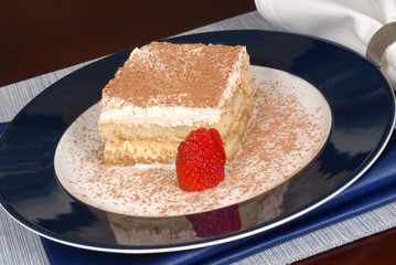 a piece of tiramisu dusted with cocoa on a blue plate
