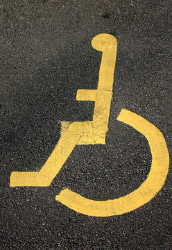 yellow sign for disabled parking on black tarmac