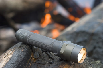 flashlight with all metal construction that is on and glowing with a fire behind