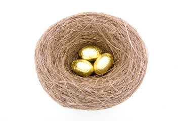 three golden choclate egg in bird's nest over whit