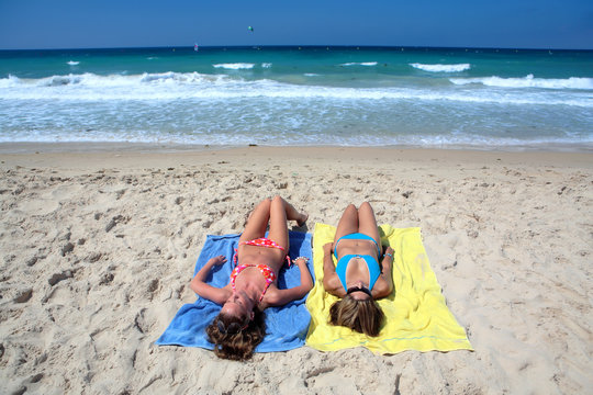 two sexy young girls laying on a sunny beach on va