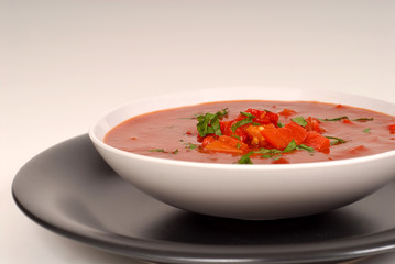 tomato, red pepper, basil soup in white bowl with light gray bac