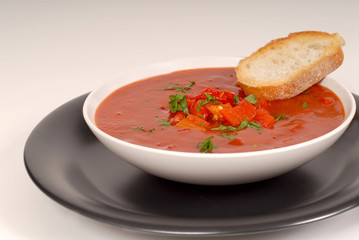 tomato, red pepper, basil soup in white bowl with bread on a lig
