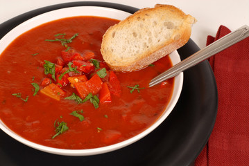 overhead view of a bowl of tomato, red pepper and basil soup wit