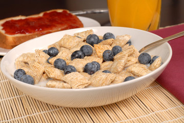 a bowl of wheat cereal with blueberries, toast and orange juice