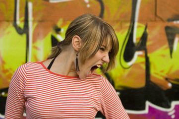 girl shouting in front of graffiti covered wall