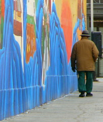 senior man in hat walking by mural