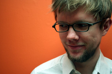 young man with glasses smiling, orange backdrop