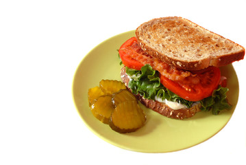 a bacon, lettuce and tomato sandwich with pickles isolated on wh