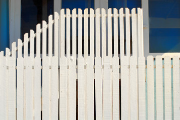 two tiered white picket fence in front of a blue building