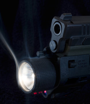 lighted semi-automated pistol with a weaponlight and red laser below with smoke