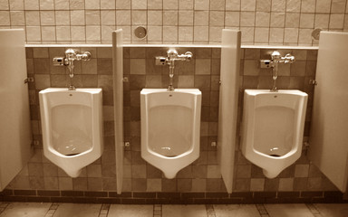 three public urinals on a tile wall in sepia as op
