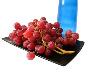 dish with grapes and blue bottle over white background