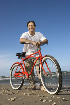 Mid-adult man leaning on red bike at beach.