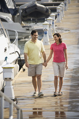 Couple holding hands and walking at harbor.