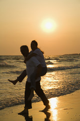 Man carrying woman on beach at sunset.