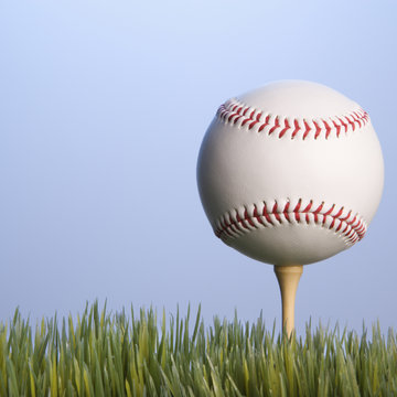baseball resting on golf tee in grass.