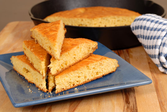 stack of cornbread on a blue plate with skillet in background