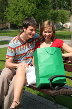 couple on park bench with shopping bag, smiling