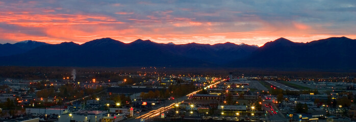 sunset over Anchorage Alaska with buildings and traffic in the foreground and mountains silhouetted...
