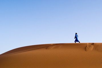 Fototapeta na wymiar Człowiek berber spaceru w wydmy Erg Chebbi o świcie