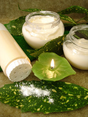 cream, bottle of powder, candle and towel with green leaves