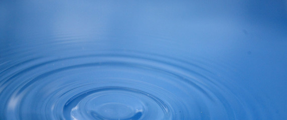 epicenter of water droplets and ripples on a blue surface of water