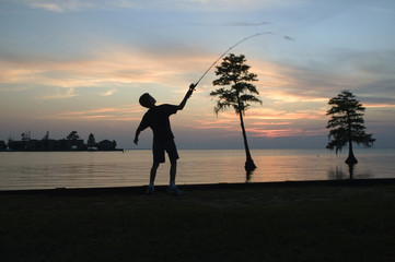 young boy fishing in a lake against sunset