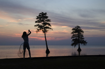 girl catching fish with a net against a beautiful sunset