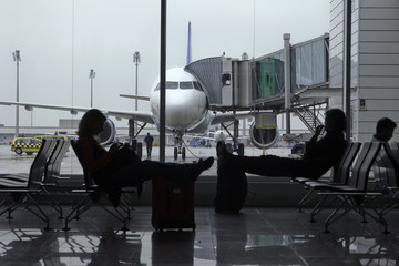Passengers in an airport terminal with a plane in background.