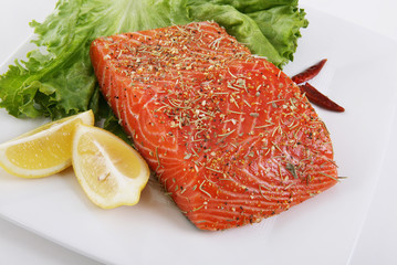 Salmon marinating on a dish with garnishments