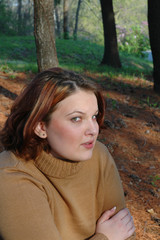 a pretty young girl sits alone in a pine tree forest.