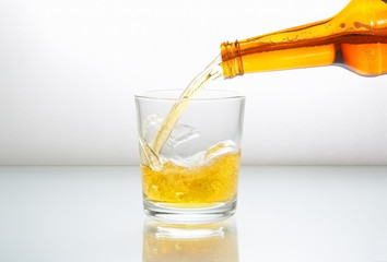 Beer pouring into glass on a white reflect background