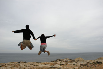 couple jump together holding hands at the coast
