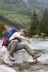 Man with backpack resting on a stone in a mountain river