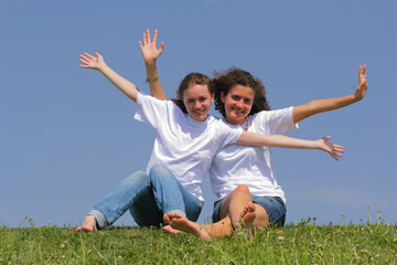 Two teen girls wave hands against a blue sky