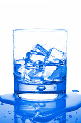 Glass of fresh liquid with ice cubes reflected on wet background