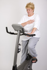 woman on excercise bike clutching chest