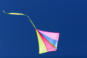 kite flying against a blue sky bright colors and streaming tail