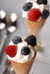 Two waffle cones with whipped cream and berries